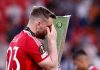 Luke Shaw berjalan melewati trofi Liga Europa