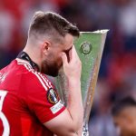 Luke Shaw berjalan melewati trofi Liga Europa