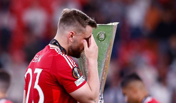 Luke Shaw berjalan melewati trofi Liga Europa